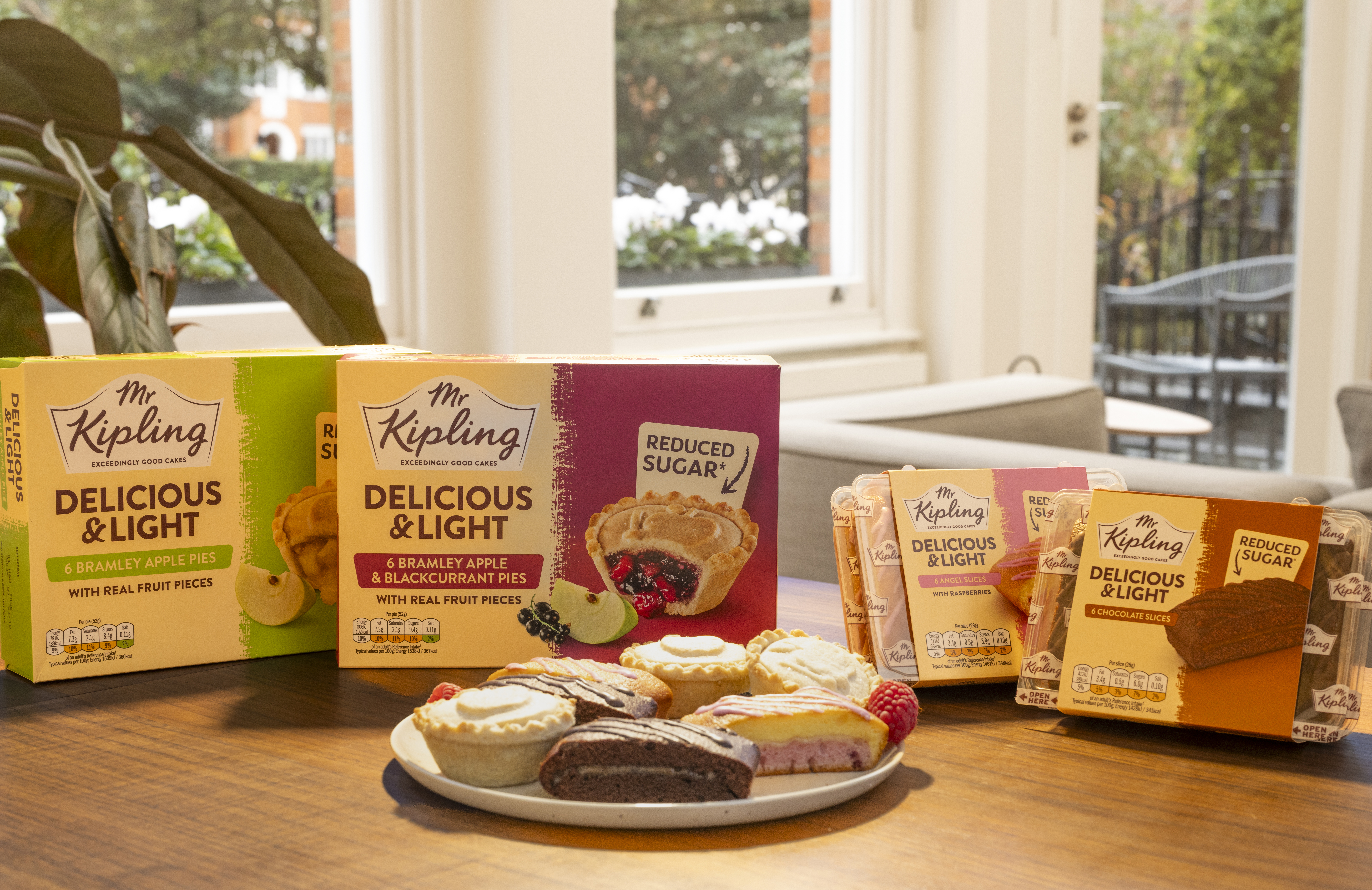 Boxes of Mr Kipling Delicious & Light fruit pies and cake slices on a table in front of a window