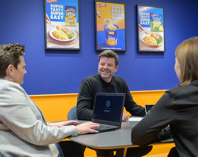 People in meeting room with laptops and brand frames on wall